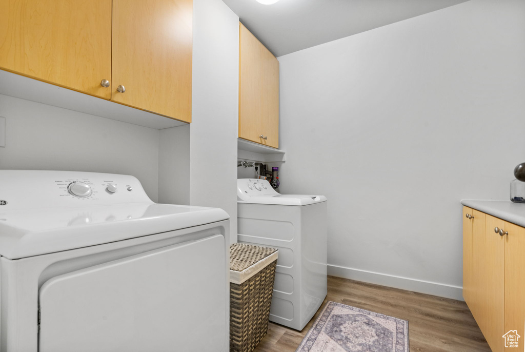 Washroom with cabinet space, independent washer and dryer, light wood finished floors, and baseboards