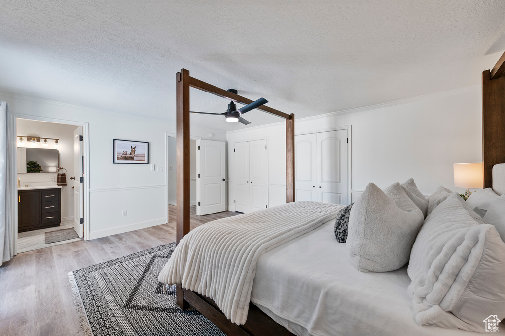 Bedroom with light wood-style floors, two closets, ornamental molding, ensuite bathroom, and baseboards