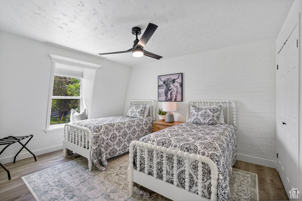 Bedroom featuring wood finished floors, a textured ceiling, a ceiling fan, brick wall, and baseboards