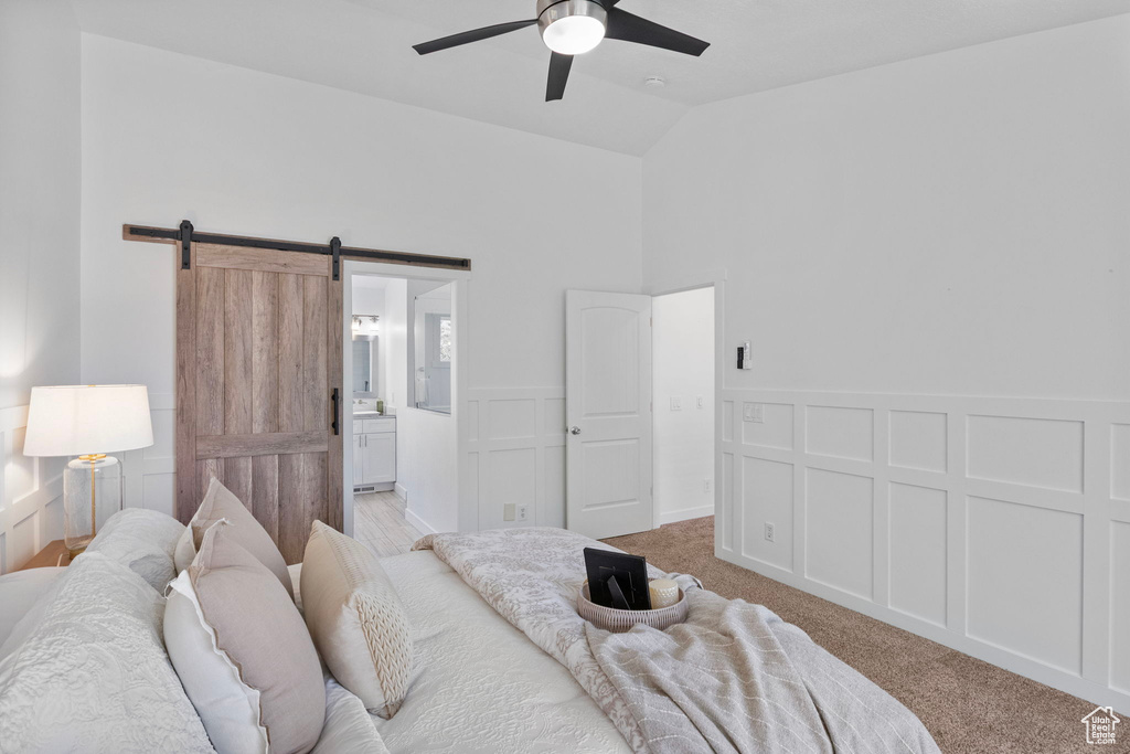 Bedroom with a barn door, light colored carpet, ensuite bath, a ceiling fan, and high vaulted ceiling
