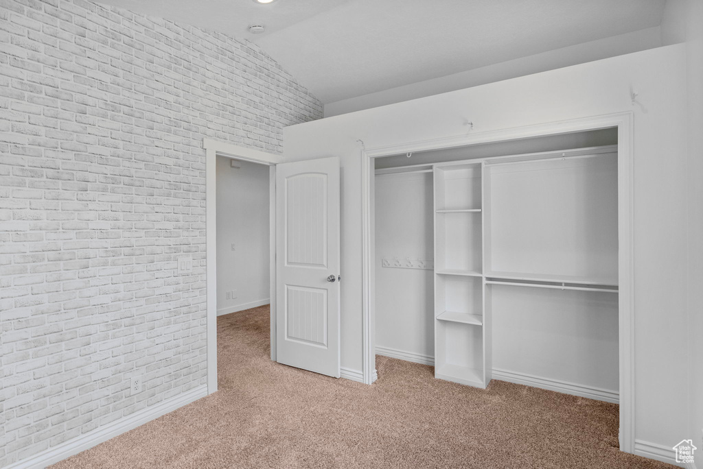 Unfurnished bedroom featuring carpet flooring, a closet, vaulted ceiling, baseboards, and brick wall