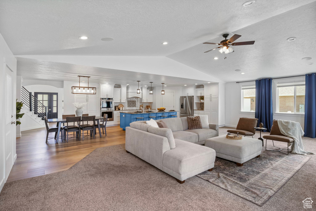 Living area featuring vaulted ceiling, a textured ceiling, a ceiling fan, light wood-type flooring, and arched walkways
