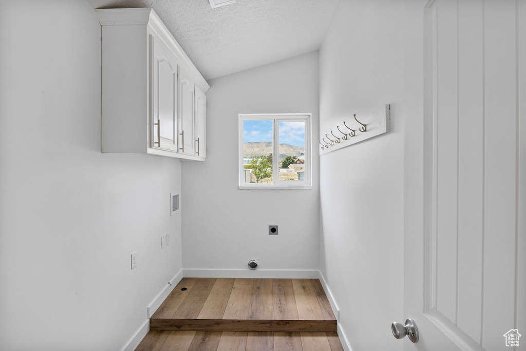 Laundry area featuring cabinet space, hookup for an electric dryer, wood finished floors, baseboards, and a textured ceiling