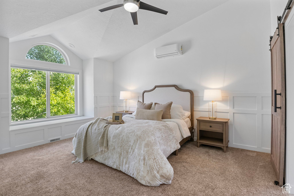 Carpeted bedroom featuring a barn door, a decorative wall, an AC wall unit, lofted ceiling, and wainscoting