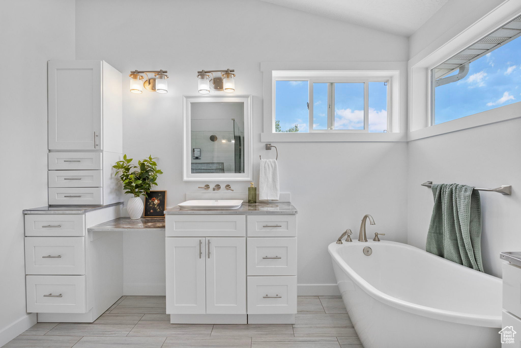 Full bathroom featuring vanity, healthy amount of natural light, a freestanding bath, vaulted ceiling, and a shower