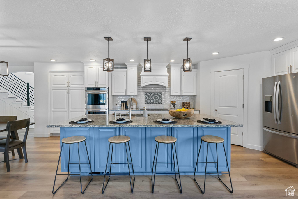 Kitchen featuring stainless steel appliances, white cabinetry, decorative backsplash, a kitchen breakfast bar, and recessed lighting
