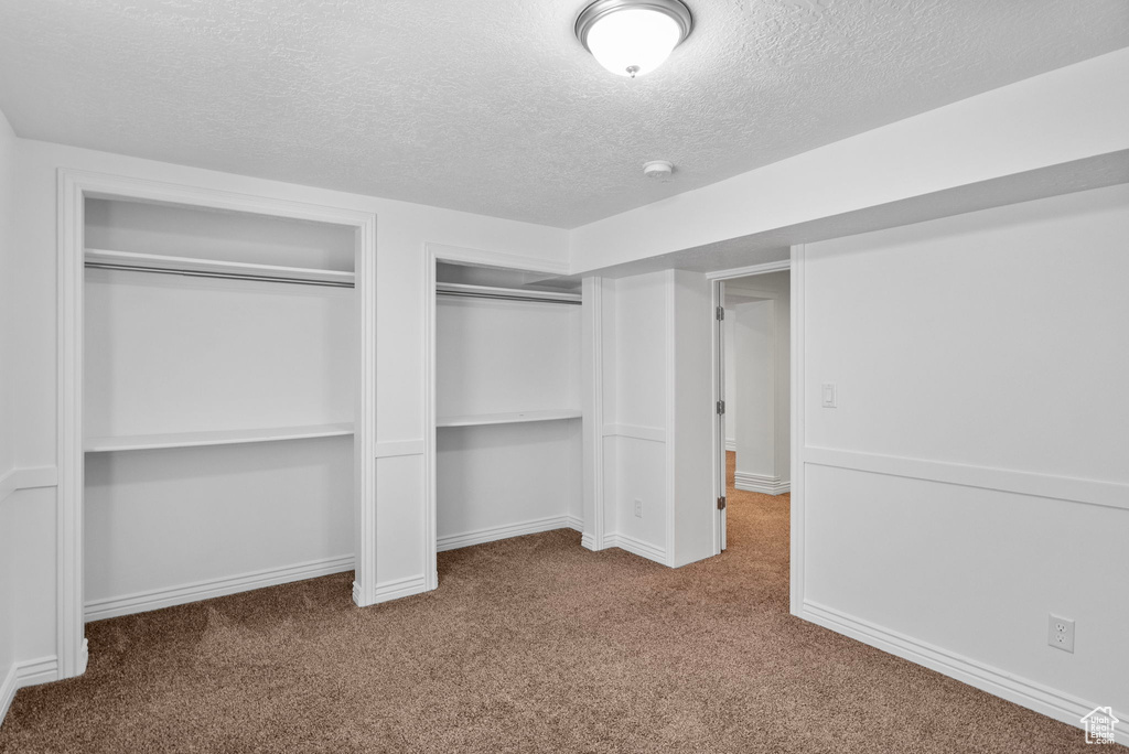 Unfurnished bedroom with a textured ceiling, carpet floors, two closets, and baseboards