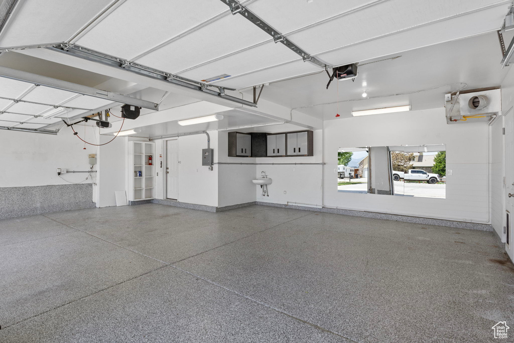 Garage featuring electric panel, a garage door opener, and baseboards