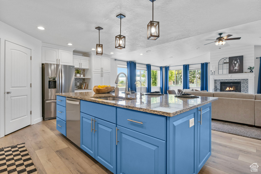 Kitchen featuring blue cabinets, a sink, appliances with stainless steel finishes, light wood-style flooring, and a textured ceiling