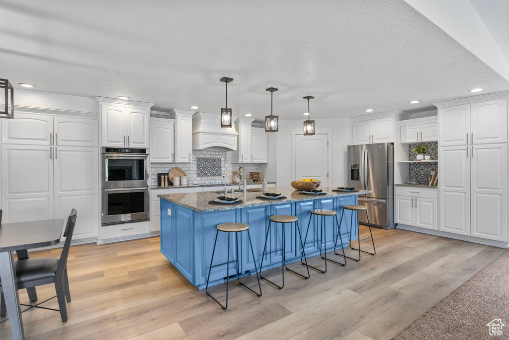 Kitchen with appliances with stainless steel finishes, white cabinets, tasteful backsplash, recessed lighting, and light wood-style flooring
