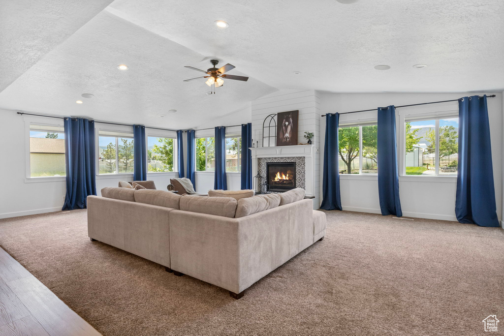 Living area with a textured ceiling, baseboards, lofted ceiling, a tiled fireplace, and ceiling fan
