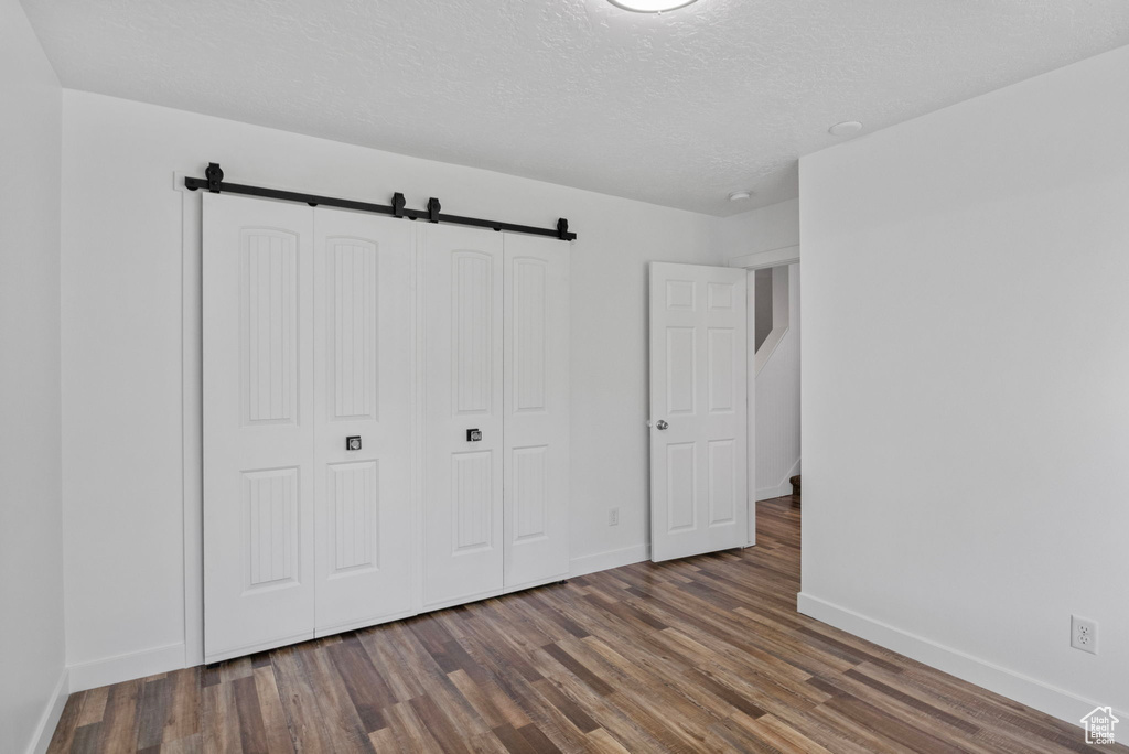 Unfurnished bedroom featuring wood finished floors, baseboards, a closet, and a textured ceiling
