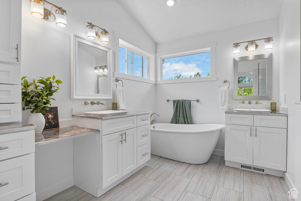 Bathroom featuring lofted ceiling, plenty of natural light, a freestanding tub, and two vanities