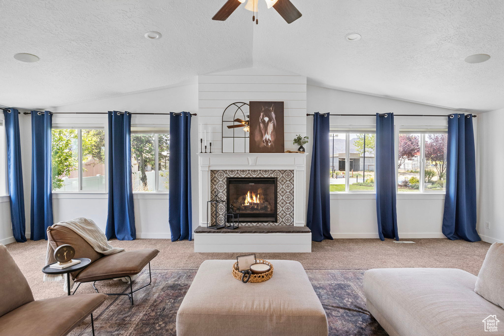 Carpeted living area with lofted ceiling, ceiling fan, a textured ceiling, baseboards, and a fireplace