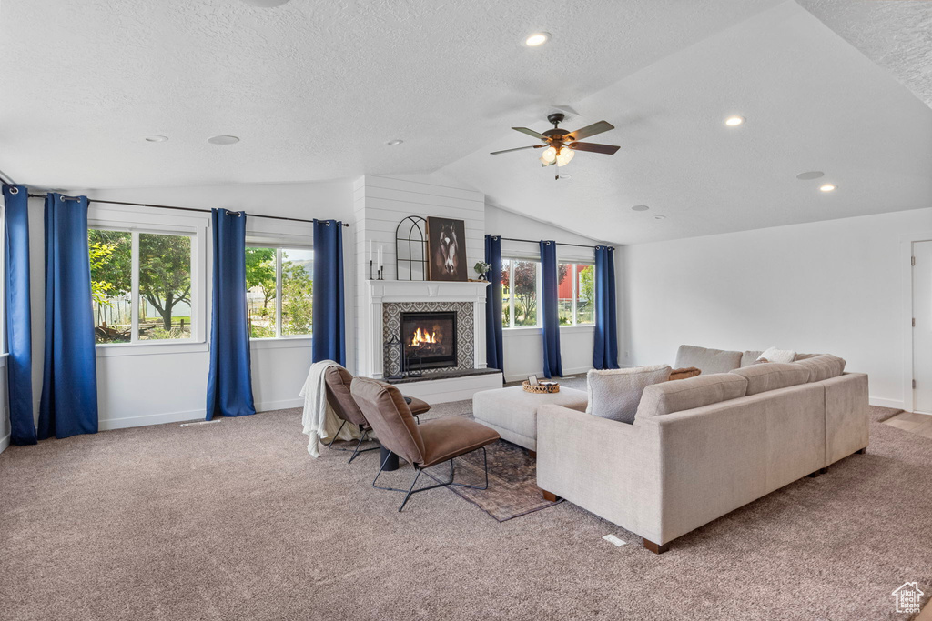 Living room with vaulted ceiling, a textured ceiling, a glass covered fireplace, ceiling fan, and carpet