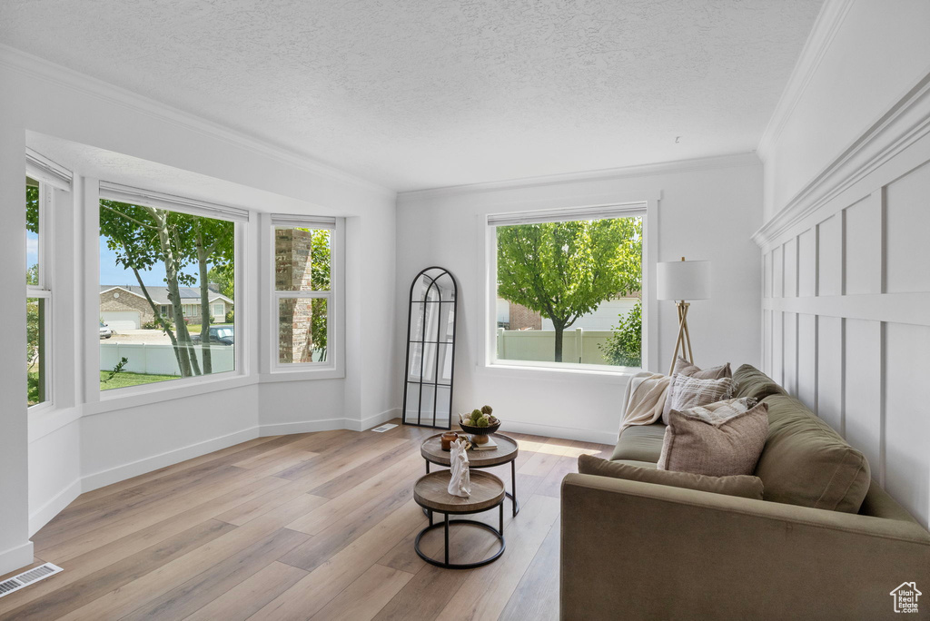 Living area with crown molding, wood finished floors, a textured ceiling, and baseboards