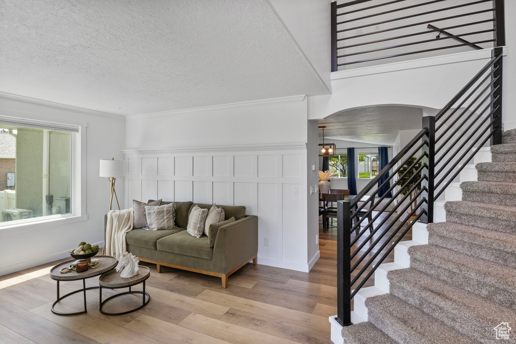 Living room with arched walkways, light wood-style floors, stairs, a textured ceiling, and crown molding