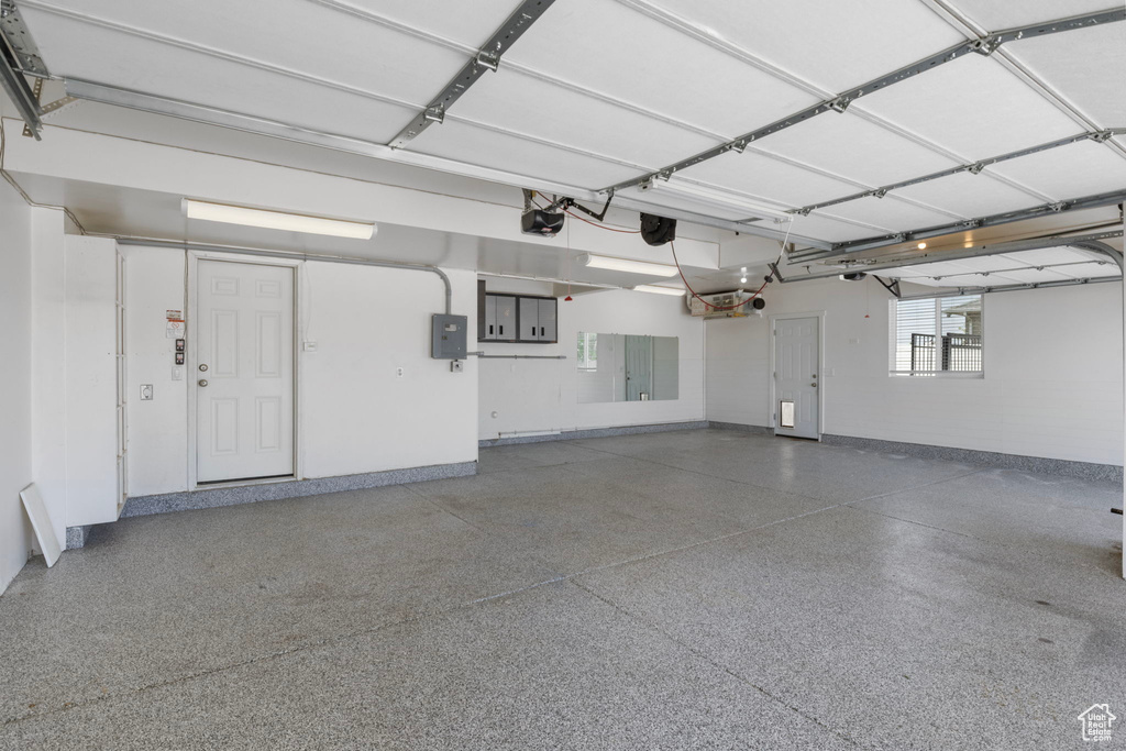 Garage featuring a garage door opener, baseboards, and electric panel