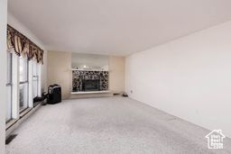 Unfurnished living room featuring a fireplace with raised hearth and carpet flooring