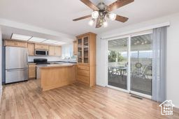Kitchen with freestanding refrigerator, light wood finished floors, glass insert cabinets, range, and a ceiling fan