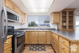 Kitchen featuring appliances with stainless steel finishes, light brown cabinetry, glass insert cabinets, and healthy amount of natural light