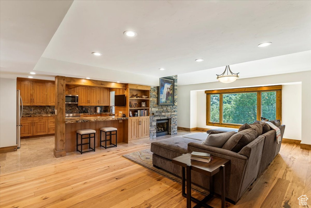 Living area with baseboards, recessed lighting, light wood-style floors, and a stone fireplace