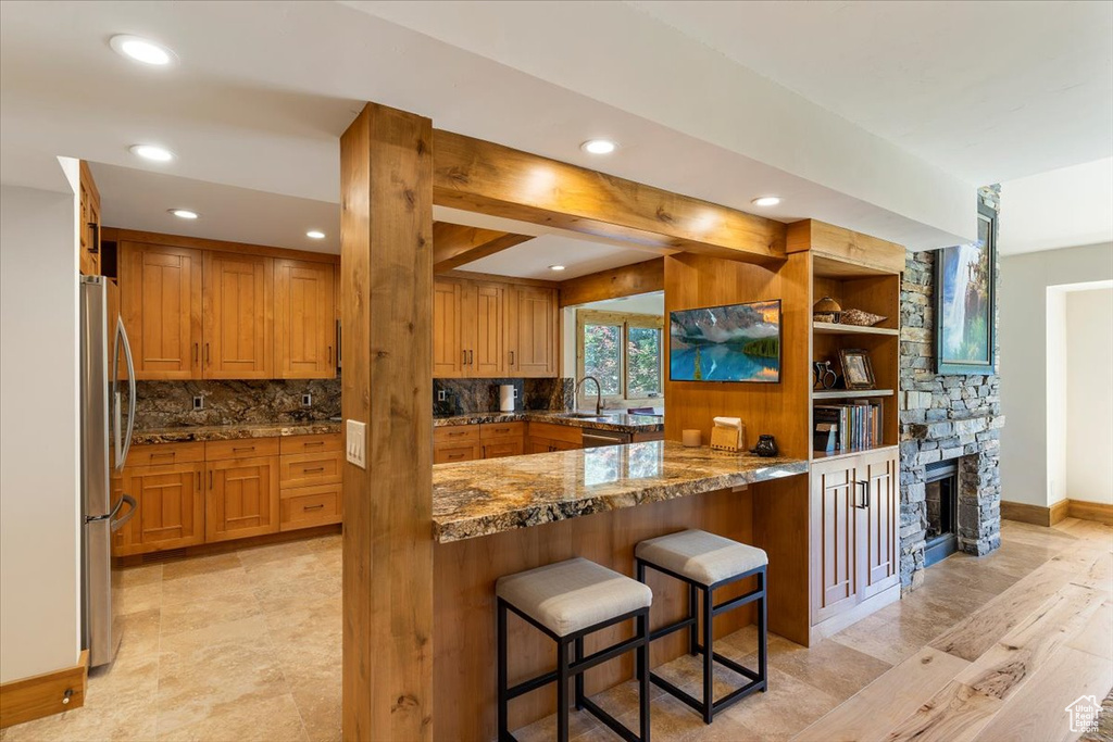 Kitchen featuring freestanding refrigerator, dark stone countertops, tasteful backsplash, a kitchen bar, and recessed lighting