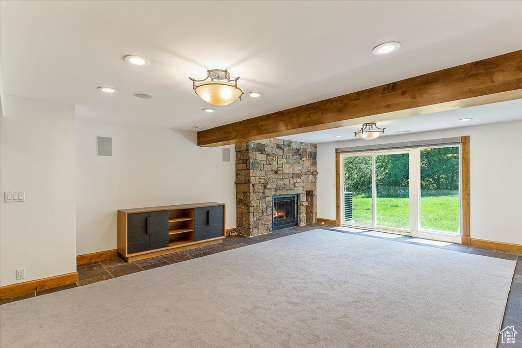 Unfurnished living room featuring recessed lighting, baseboards, a stone fireplace, beam ceiling, and dark carpet