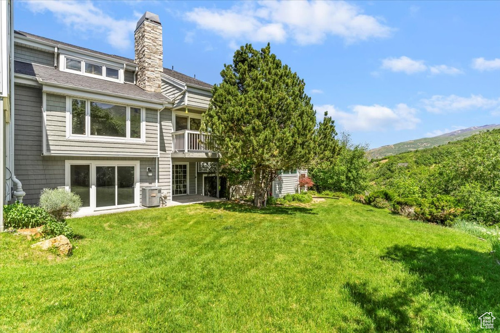 Back of house with a chimney, a yard, a cooling unit, a shingled roof, and a mountain view