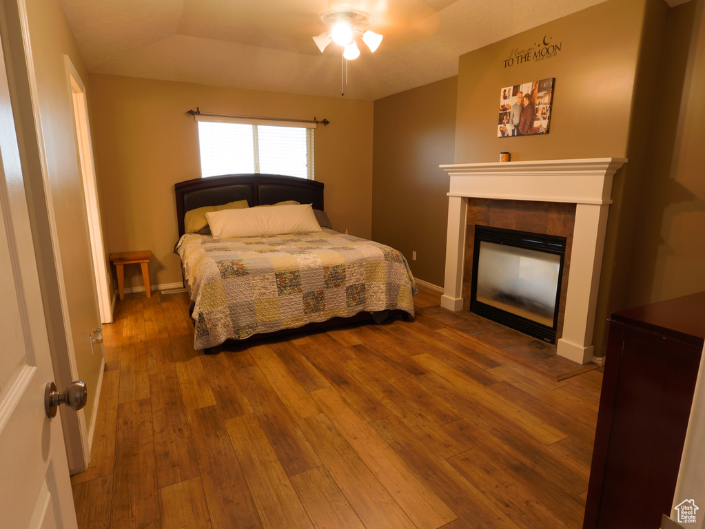 Bedroom with hardwood / wood-style flooring, a tile fireplace, baseboards, and a ceiling fan