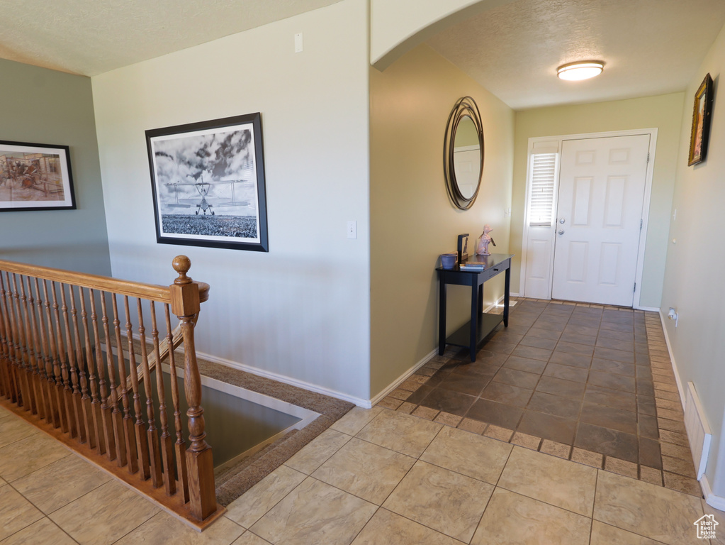 Tiled entrance foyer with arched walkways, baseboards, and a textured ceiling