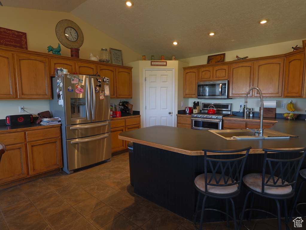 Kitchen featuring stainless steel appliances, brown cabinetry, a sink, a kitchen bar, and lofted ceiling