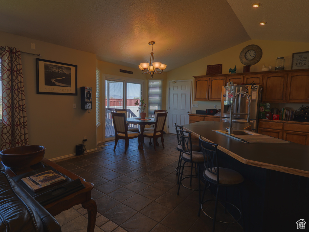 Kitchen featuring a chandelier, stainless steel refrigerator with ice dispenser, lofted ceiling, baseboards, and a kitchen breakfast bar