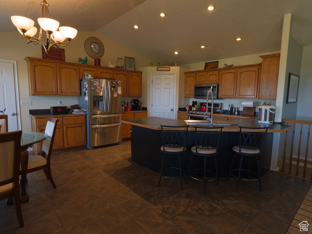 Kitchen featuring appliances with stainless steel finishes, brown cabinetry, a peninsula, a kitchen breakfast bar, and vaulted ceiling