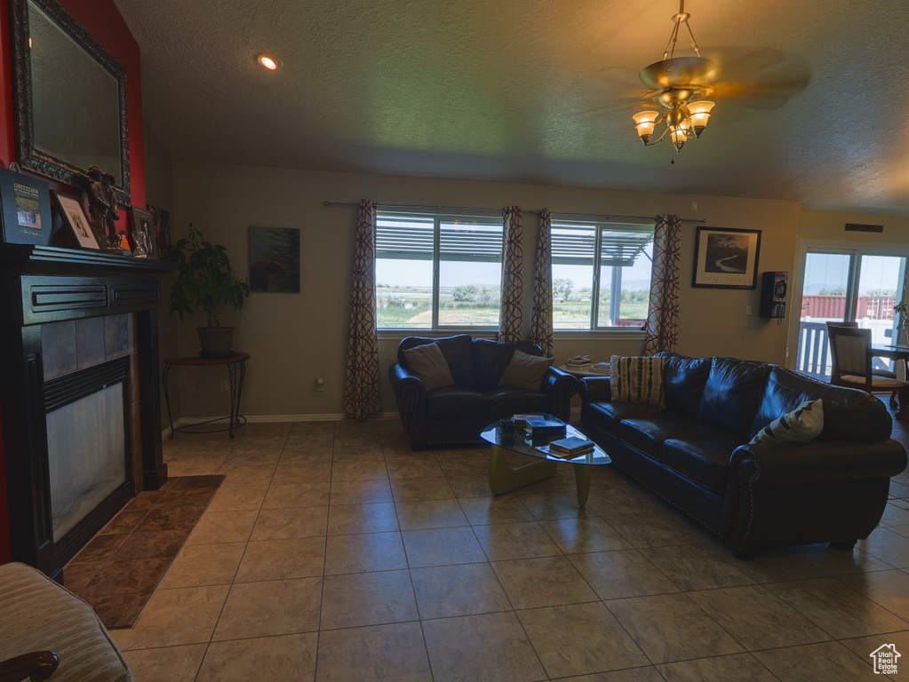 Tiled living room featuring plenty of natural light, a ceiling fan, a fireplace, baseboards, and a textured ceiling