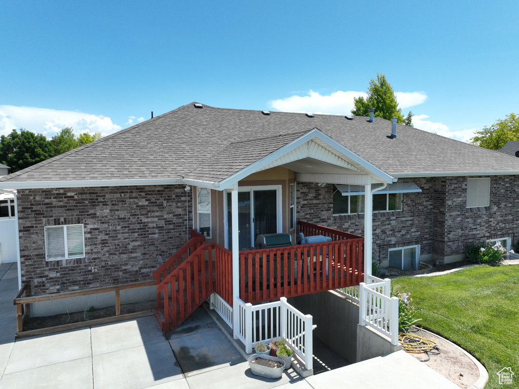 Rear view of property with brick siding, a shingled roof, a yard, a deck, and a patio
