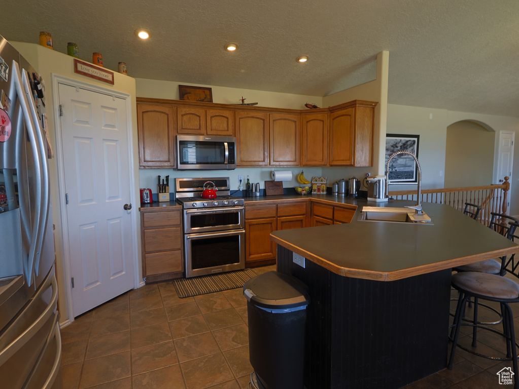 Kitchen featuring appliances with stainless steel finishes, a sink, a kitchen bar, a peninsula, and arched walkways