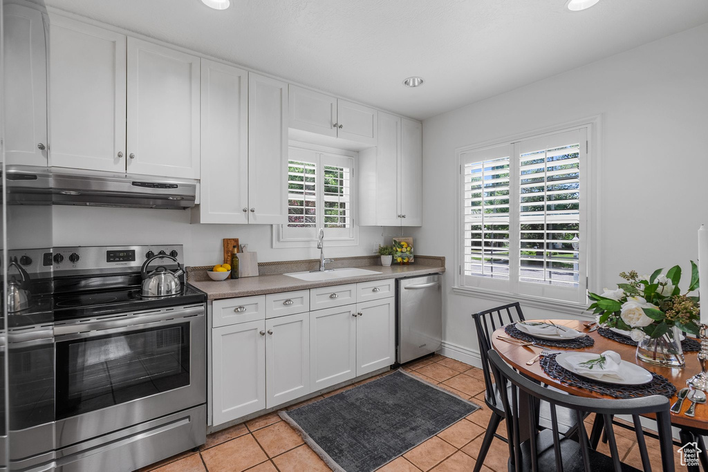 Kitchen with stainless steel appliances, under cabinet range hood, a sink, and white cabinetry