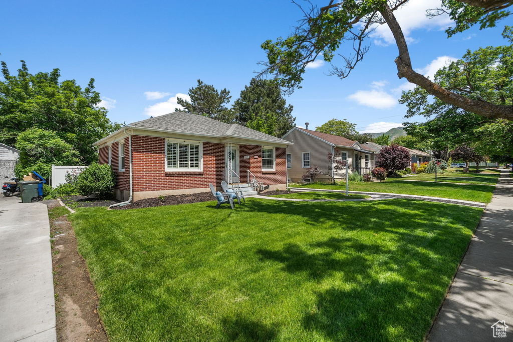 View of front of property with brick siding, entry steps, a front yard, and roof with shingles
