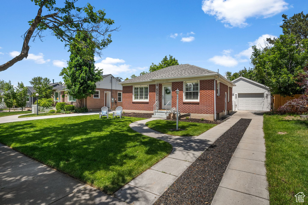 Bungalow with brick siding, an outbuilding, a front lawn, concrete driveway, and a garage