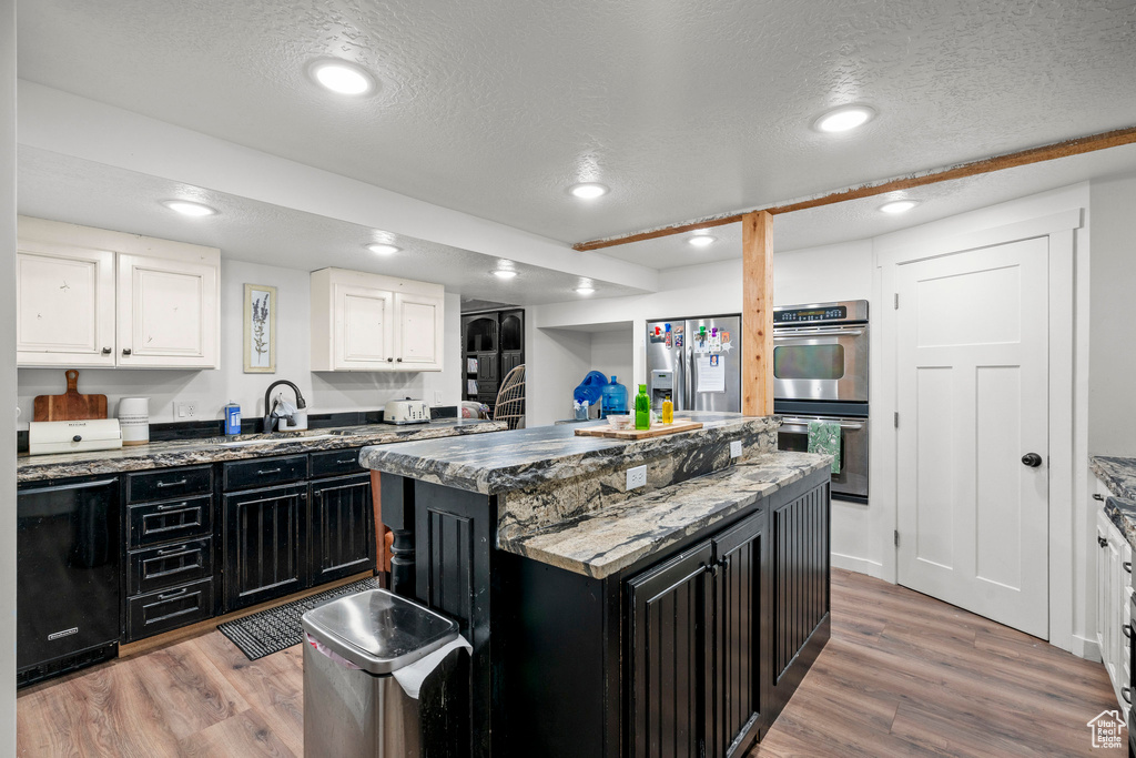 Kitchen featuring appliances with stainless steel finishes, dark cabinetry, light wood-style floors, a textured ceiling, and recessed lighting