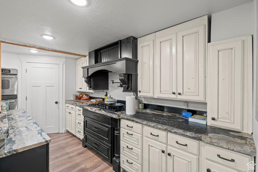 Kitchen with stainless steel double oven, white cabinets, a textured ceiling, light wood finished floors, and gas cooktop