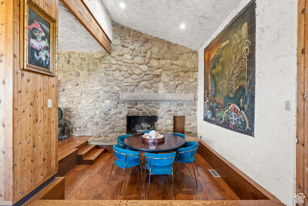 Dining space with vaulted ceiling, hardwood / wood-style flooring, a stone fireplace, and baseboards