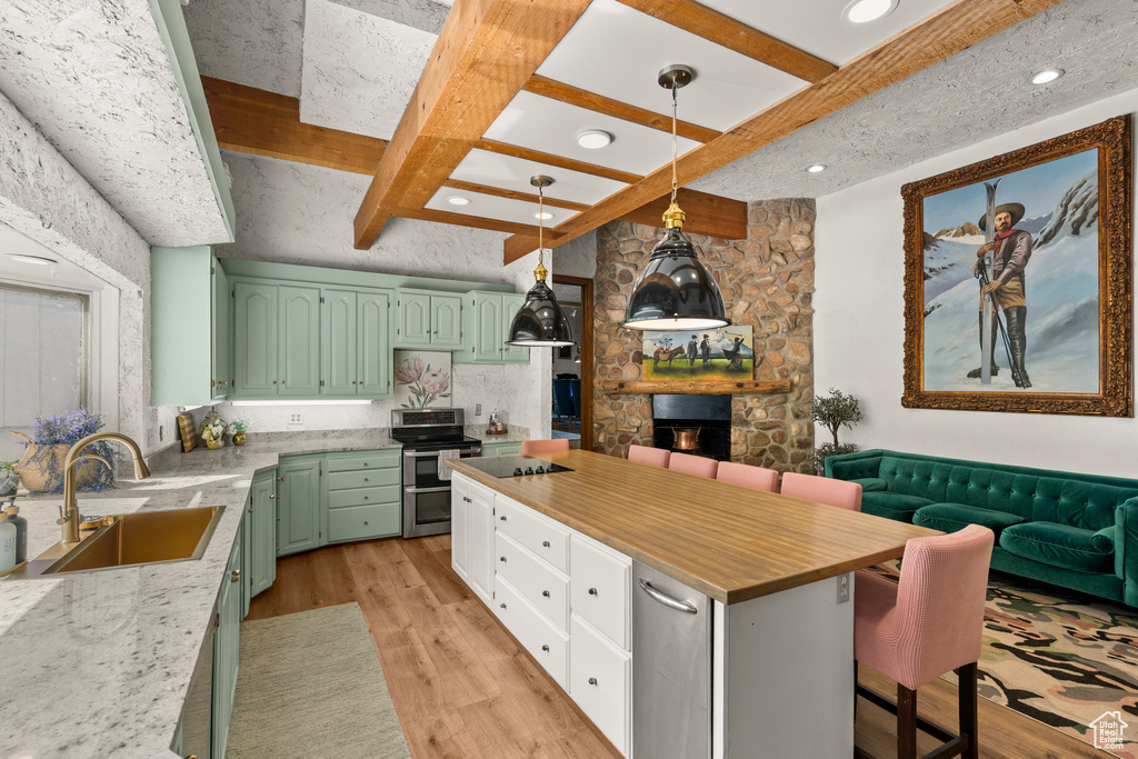 Kitchen with green cabinets, double oven range, a sink, a stone fireplace, and light wood finished floors