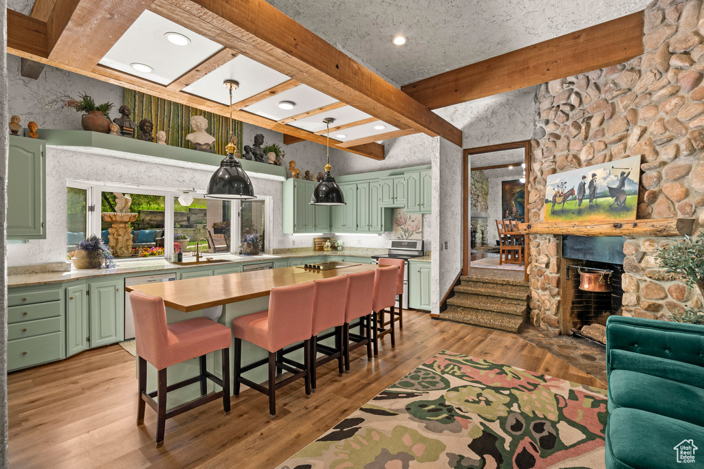 Kitchen with green cabinets, beam ceiling, light countertops, light wood-style flooring, and hanging light fixtures