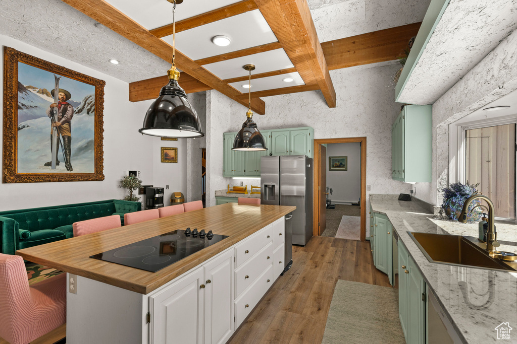 Kitchen featuring green cabinets, a sink, stainless steel fridge, black electric cooktop, and light wood-type flooring