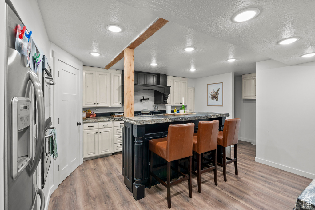 Kitchen featuring a textured ceiling, light wood-type flooring, stainless steel fridge, baseboards, and a kitchen bar