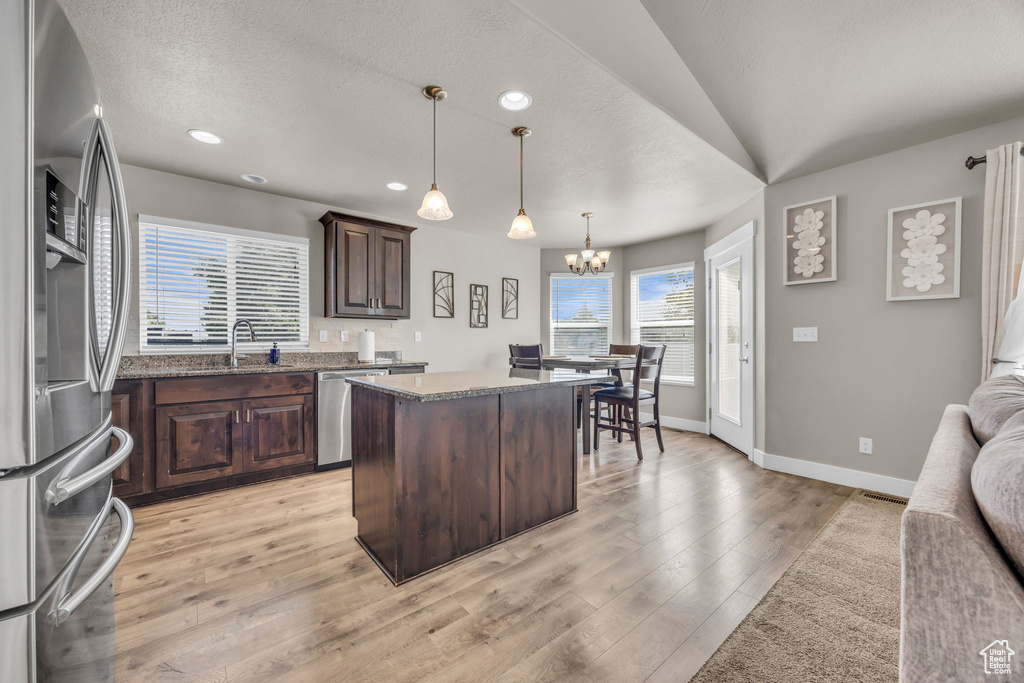 Kitchen featuring appliances with stainless steel finishes, dark brown cabinets, a chandelier, baseboards, and a center island