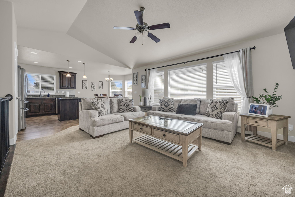 Carpeted living room with ceiling fan, vaulted ceiling, and a chandelier