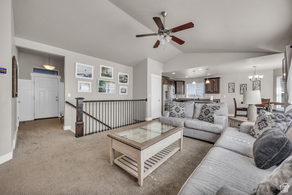 Living area featuring vaulted ceiling, ceiling fan, a chandelier, and light carpet